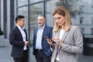 A successful and experienced business woman outside the office building is reading from a tablet computer, an employee with colleagues in business suits on a break photo