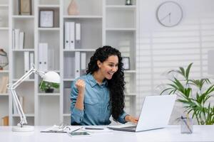 alegre Hispano mujer trabajando desde hogar, celebrando un negocio logro en su acogedor hogar oficina configuración. foto