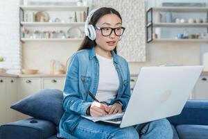 Young beautiful Asian woman studying at home remotely, female student listening to online course photo