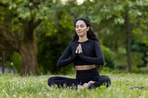 A serene Hispanic woman in a lotus pose meditates in a tranquil park setting, embodying peace and mindfulness. photo