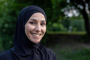 retrato de un contento musulmán mujer vistiendo un hijab al aire libre con un natural verde fondo, exhibiendo cultural diversidad y alegría. foto