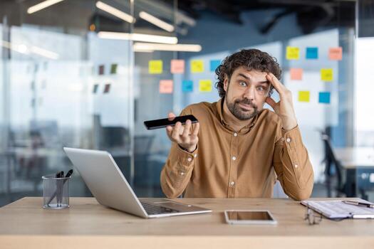 A mature businessman appears confused while using a smartphone in a modern office setting. Problem-solving concept. photo