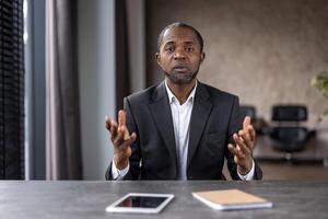 A mature businessman engages in a discussion in a well-lit office setting. His expression is serious as he talks, with digital devices nearby. photo