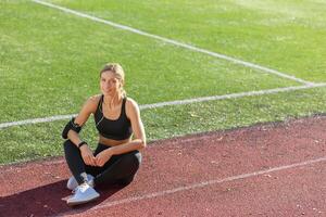 deportivo mujer disfrutando descanso hora sentado en pista campo en Brillo Solar después hacer ejercicio, exhibiendo sano estilo de vida. foto