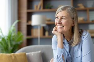 A contemplative adult woman sits on a couch, surrounded by soft, cozy pillows, lost in thought in a serene living room setting. photo