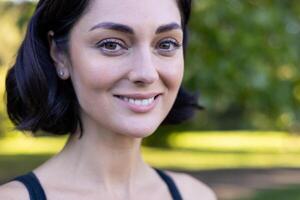 Close-up of a cheerful young woman smiling in nature with sunlight filtering through the trees. photo