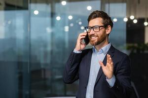 Mature businessman in a business suit talking on the phone, the manager is satisfied with the result of the achievement and work talks about the positive result, the man is at work inside the office. photo