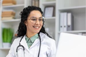 A joyful Latina doctor wearing glasses smiles cheerfully at work, radiating positivity and confidence in a clinical setting. photo