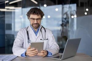 un alegre masculino cuidado de la salud profesional es comprometido con un digital tableta en un bien iluminado contemporáneo oficina espacio, simbolizando médico tecnología integración. foto