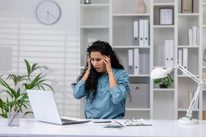 Worried Hispanic businesswoman receiving bad news while working from her home office, showing confusion and stress. photo