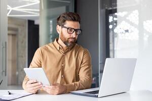 Serious concentrated man working inside office with tablet computer, thinking mature businessman using laptop, reading data, and checking online report financial data. photo