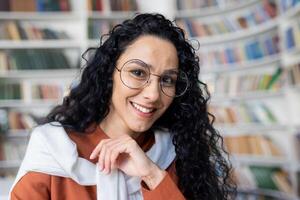 Portrait of happy young Indian female teacher sitting in school classroom smiling and looking at camera, concept of online lessons, cheerful tutor. photo