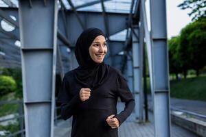 un alegre musulmán mujer vistiendo un hijab disfruta un correr en un urbano parque configuración, exudando salud y felicidad. foto