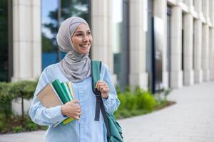 A cheerful young Arab woman in a hijab holding notebooks, walking by an office, exuding confidence and professionalism. photo