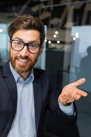 vertical disparo, un empresario en el oficina es hablando a colegas y amigos utilizando un solicitud en un teléfono inteligente, un maduro hombre en un negocio traje dentro el oficina es sonriente amigable. foto