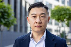 A professional portrait of an Asian businessman in a suit, conveying confidence and determination, taken outdoors. photo