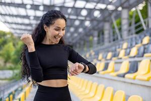 centrado en el fitness mujer en atlético vestir utilizando un reloj inteligente a un Deportes estadio, encarnando salud y activo estilo de vida. foto