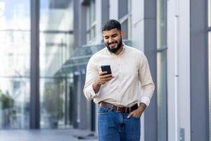 sonriente joven hombre utilizando teléfono inteligente en urbano ajuste foto