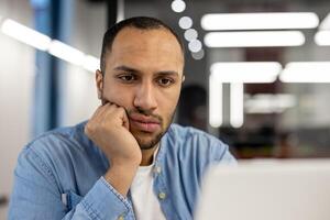 un masculino oficina trabajador es capturado en un sincero momento de contemplación. él aparece enfocado y introspectivo, sugerencia profundo pensamiento o resolución de problemas a su lugar de trabajo. foto