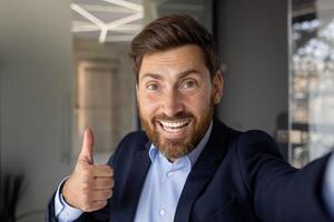 A young handsome businessman man talks online via call, shows the super gesture with his finger on the gadget camera. photo