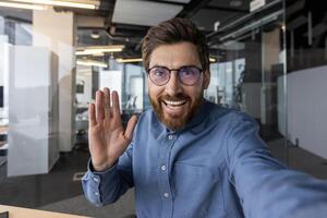 A welcoming professional male greeting with an open hand in a well-lit, contemporary office setting, conveying openness and friendliness. photo