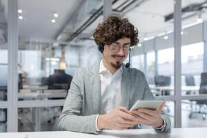 Experienced young adult businessman working inside an office, showcasing professionalism with a content emotional state and multitasking abilities. photo