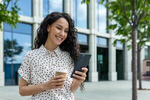 A young woman holding a coffee cup and texting on her phone with modern buildings in the background during the day. photo