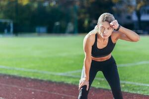 Tired sportswoman resting after jogging on a sunny day at the stadium, blonde in sportswear taking a breather. photo