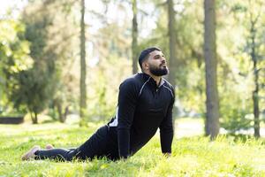 Active man enjoying a stretch in peaceful green park surroundings, with sunlight filtering through the trees. photo