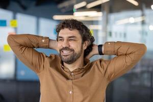 relajado caucásico masculino extensión espalda y descansando cabeza en manos mientras observando oficina vida desde gabinete. satisfecho ejecutivo acuerdo equilibrar de estrés y haciendo descanso desde trabajo para descansando foto