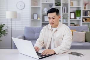 Serious and focused Asian man, businessman, freelancer, student working studying at home using laptop, Sitting at table and talking on call, typing. photo