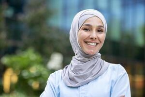 Portrait of a joyful young woman wearing a hijab, with a modern city background. Emphasizing diversity and happiness. photo