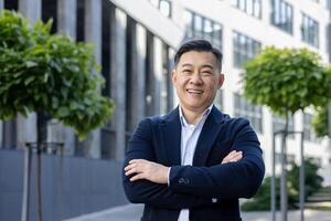 retrato de un alegre asiático empresario con brazos cruzado, con confianza sonriente en un urbano ambiente. foto