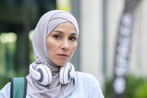 un pensativo mujer vistiendo un hijab y auriculares, mirando calma, capturado con un suave atención antecedentes en un urbano ajuste. un imagen transporte moderno estilo de vida y tranquilidad. foto
