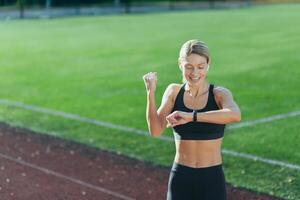 Satisfied with the result of training and running, the athlete looks at the smart watch, the blonde holds her hand up and celebrates the victory. photo