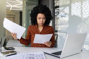 Upset and unsatisfied woman at workplace, businesswoman boss checking documents, accounts and contracts, financial woman got bad results in financial reports, working inside office with laptop. photo