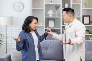 Family quarrel, asian couple man and woman yelling at each other, family conflict, asians at home standing angry in living room. photo