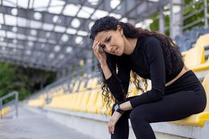 An athletic woman in sportswear taking a rest on yellow stadium seats after exercising. Concept of fitness and healthy lifestyle. photo