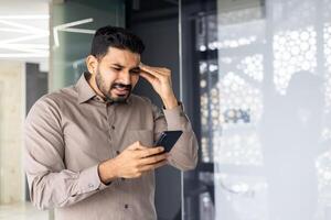 un hombre es mirando a su célula teléfono con un preocupado expresión en su cara foto