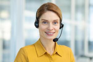Portrait of successful smiling business woman with headset phone, mature experienced worker smiling and looking at camera, call online meeting, online customer support service. photo