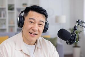 Friendly Asian man wearing headphones in a home environment, engaging in a call with a positive expression, looking into the camera. photo