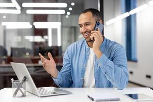 Cheerful businessman engaged in phone conversation at a modern office desk, displaying positivity and professionalism. photo