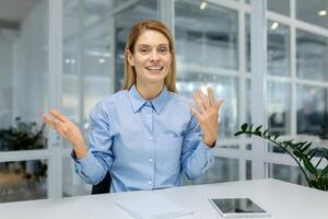 A professional woman in a blue shirt gestures animatedly while looking at a camera, implying a call discussion. photo