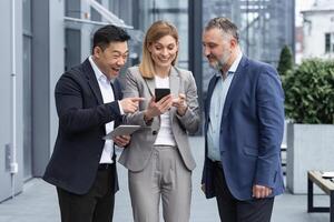 Tres colegas empleados reloj gracioso s o Mira a fotos, imágenes recuerdos mirando a teléfono inteligente pantalla utilizando móvil teléfono. grupo de negocio personas oficina trabajadores teniendo divertido en rompe foto