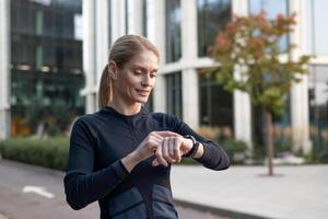 A focused female athlete pauses during her urban workout to monitor her performance on a smartwatch. Capturing a moment of technology integrating with fitness in a city environment. photo