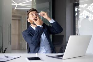 A young businessman sits in the office at the desk and instills medicine into his eye for inflammation and fatigue, cleans the lenses. photo