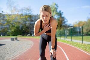 cansado mujer atleta atrapando su aliento Después del ejercicio en un pista campo, ilustrando aptitud agotamiento y determinación. foto