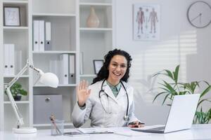 Cheerful Hispanic female doctor waving hand in greeting at her office, representing approachable healthcare professionals. photo