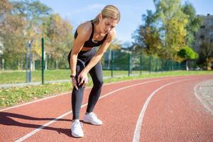 Female athlete in sportswear pausing her exercise due to a painful knee injury on a sunny outdoor track. photo