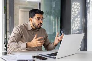 trastornado y decepcionado empresario a lugar de trabajo tiene negativo financiero resultados, insatisfecho hombre trabajando dentro oficina a lugar de trabajo con ordenador portátil. foto